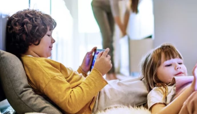 Kinder beim Hinlegen mit Tablets, während die Mutter im Hintergrund die Küche putzt